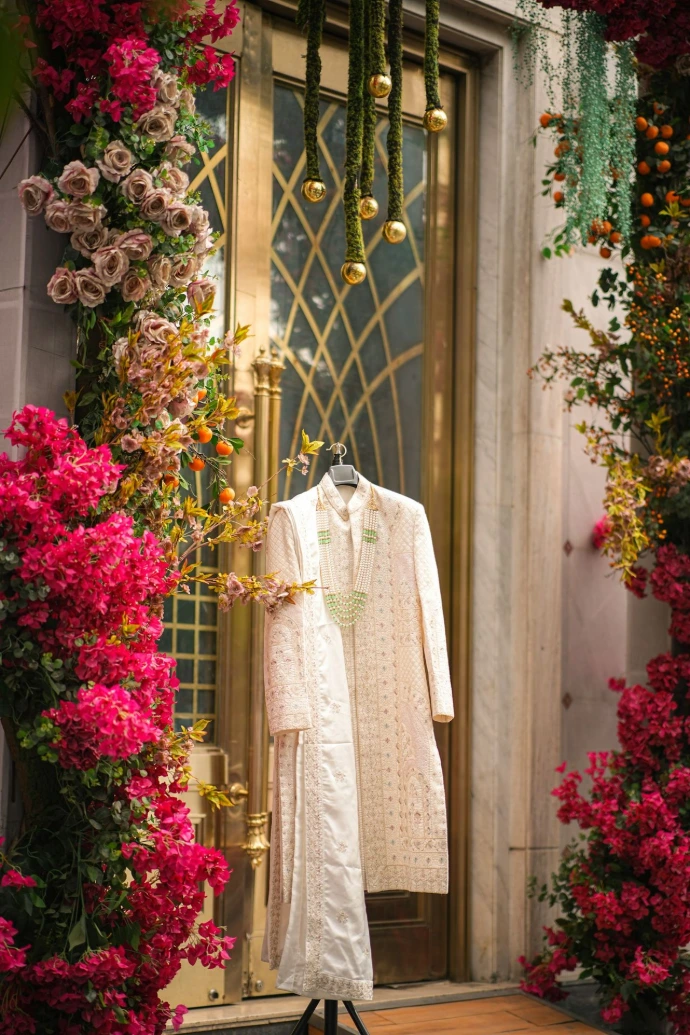 Cream sherwani hangs before golden door adorned with vibrant flowers